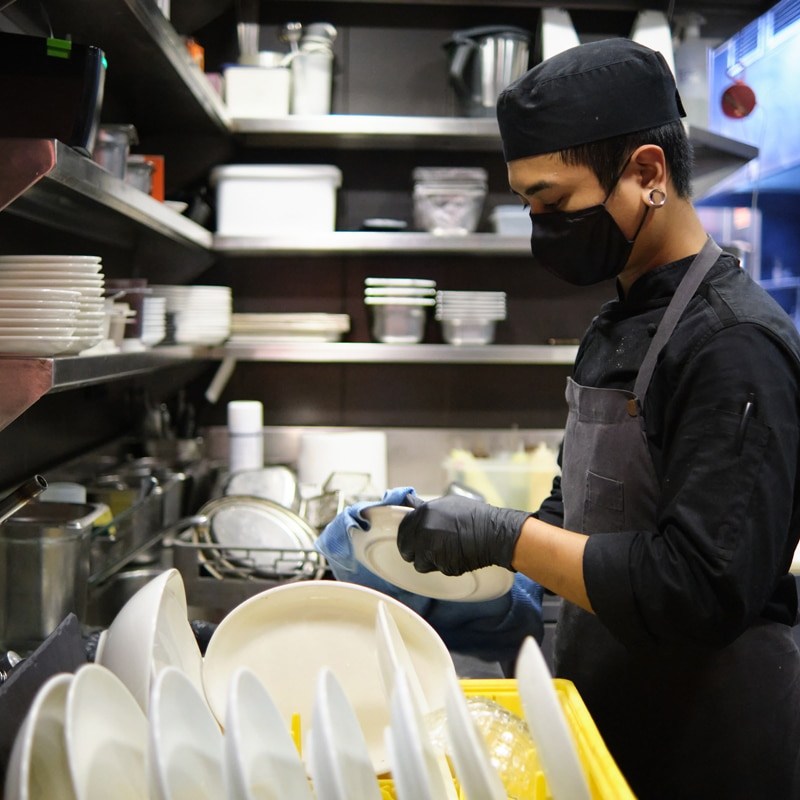 Worker cleaning dishes at restaurant kitchen.